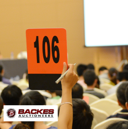 Image for Woman's hand holding up an auction card with the number 106 on it in a full auction room