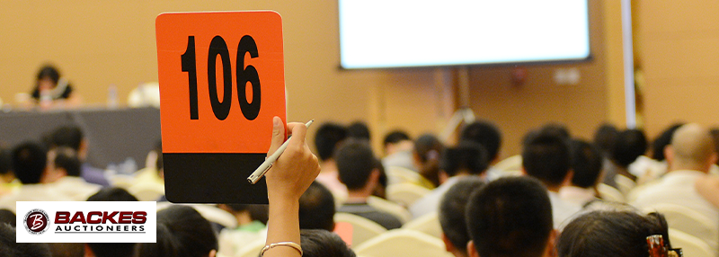 Image for Woman's hand holding up an auction card with the number 106 on it in a full auction room