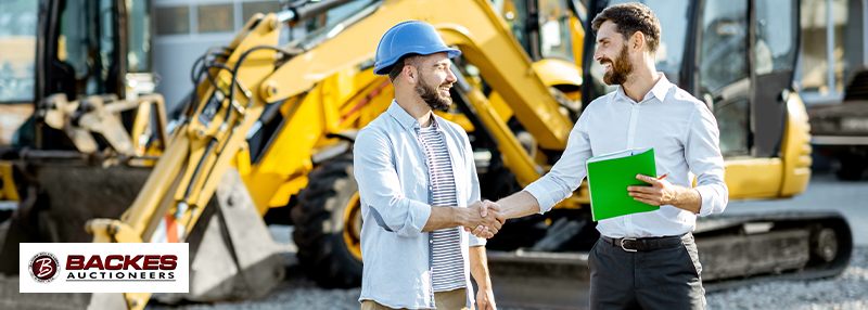 Image for Two men shaking hands outdoors in front of some construction equipment