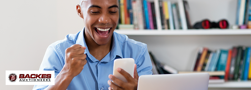 Image for Happy young man holding his phone and raising a fist due to excitement 