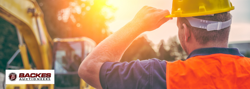 Image for Man with hard hat and orange vest looking on to construction equipment